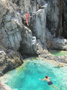 two people jumping off rocks into the water