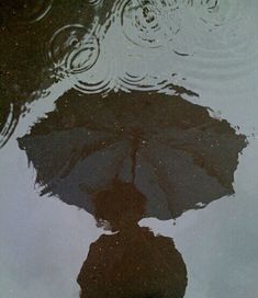 a person standing in front of a puddle with an umbrella on the ground next to it