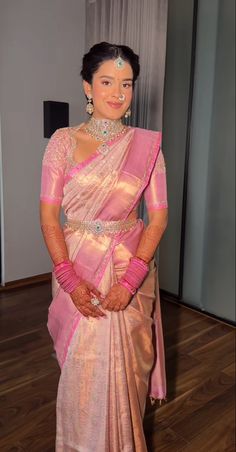 a woman in a pink and gold sari posing for the camera with her hands on her hips