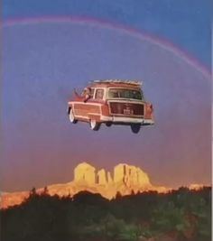 an old car is flying in the air with a rainbow behind it and mountains below