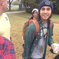 a group of young people standing around each other in a field with backpacks and coffee cups