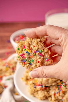 a hand holding a cookie with sprinkles on it and some milk in the background