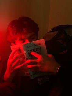 a man reading a book in the dark with red light coming from his eyes and hands