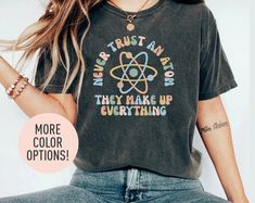 This Never Trust An Atom They Make Up Everything Shirt is the perfect birthday gift or Christmas gift for all women! All of our shirts are made with the highest quality materials and are super soft and cozy! 💚 HOW TO ORDER 💚 1. Check our photos for sizing and color options. 📏 2. Choose your quantity.  Feel free to add as many shirts as you wish! ✨ 3. Select your size and color from the drop-down menus. ✨ 4. Click "ADD TO CART" to add the shirt to your virtual cart. 🛒 5. Click "PROCEED TO CHE Trendy Graphic Print Shirt As Gift, Trendy Slogan Tops For Gifts, Retro Letter Print Tops For Gifts, Retro Letter Print Tops As Gift, Trendy Text Print Top As Gift, Casual Shirt With Funny Text As Gift, Trendy Crew Neck Shirt As A Gift, Trendy Crew Neck Shirt As Gift, Trendy Tops For Mother's Day Gift