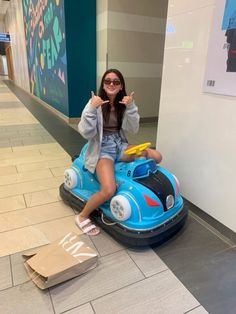 a woman sitting on top of a toy car in the middle of an airport lobby