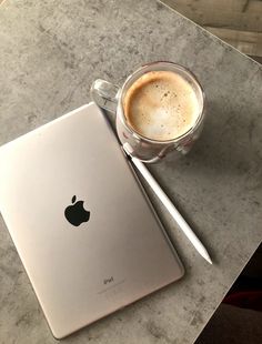 an apple ipad next to a cup of coffee on a marble counter top with a pen and paper