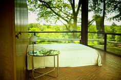 a bed sitting on top of a wooden floor next to a glass table with a lamp