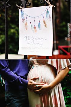 a pregnant woman holding her belly in front of a sign with feathers hanging from it