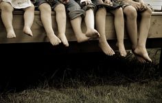 four children sitting on a wooden bench with their feet hanging off the back of them