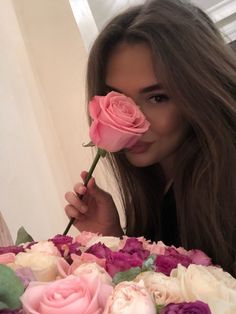 a woman holding a pink rose in front of her face and looking at the camera