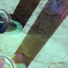 two wine glasses sitting on top of a marble table next to each other with their shadows