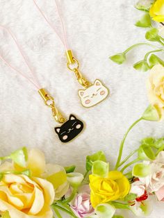 two necklaces with cats on them sitting next to flowers