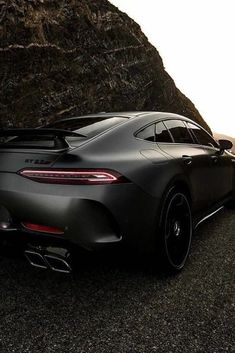 the rear end of a black sports car parked in front of a large rock formation