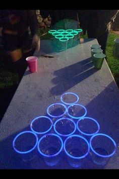 several cups are lined up on a table with neon lights in the background and people standing around