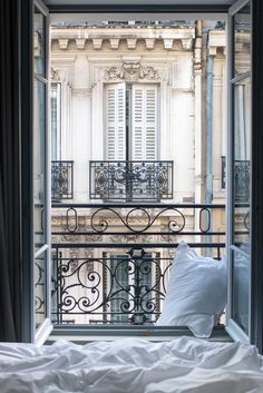 an open window overlooking a balcony with iron railings and white pillows on the bed