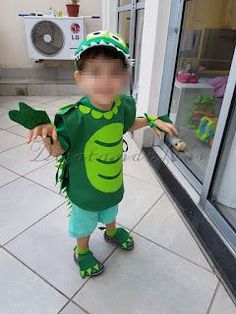 a little boy dressed up as a green peael costume standing in front of a store window