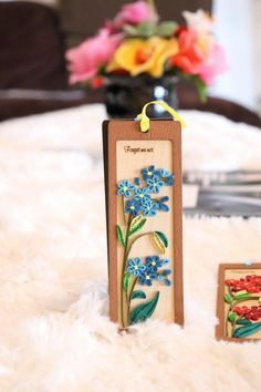 a wooden plaque with blue flowers on it next to a vase filled with red and yellow flowers