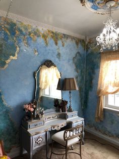 a desk with a mirror and lamp in front of a blue painted wall that has peeling paint on it