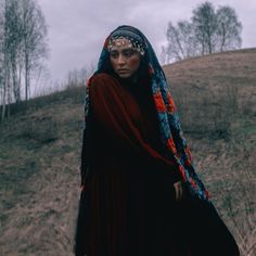 a woman wearing a red and blue headdress standing on top of a hill