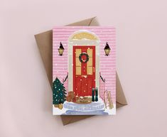 a pink card with a red door and christmas tree on the front, in front of a pink background