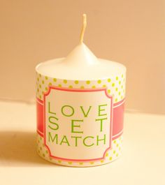 a small white candle sitting on top of a table next to a cup with the words love set match written on it