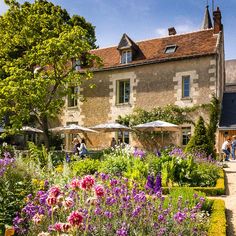 an outdoor garden with flowers and people in the background, surrounded by stone buildings on either side