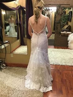 a woman standing in front of a mirror wearing a wedding dress with an open back