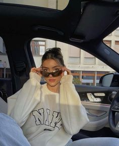 a woman sitting in the passenger seat of a car wearing sunglasses and a sweatshirt with letters on it