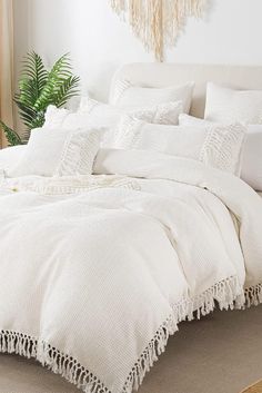 a bed with white linens and pillows in a room next to a potted plant