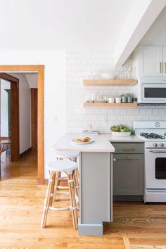 a kitchen with white and gray cabinets, wood flooring and open shelving above the stove