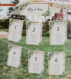 wedding seating cards hanging from a line in the grass with flowers and greenery on them