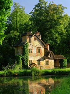 an old house with ivy growing on it's roof next to the water and trees