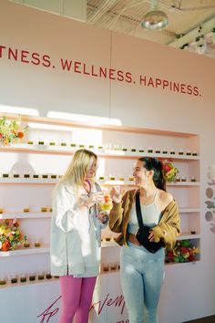 two women standing next to each other in front of a wall with flowers on it