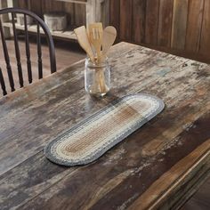 a wooden table topped with a jar filled with utensils and a rug on top of it