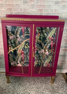 a pink cabinet with tropical print on the front and bottom, sitting against a brick wall