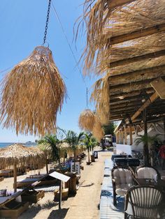 an outdoor dining area with straw umbrellas and chairs on the side of the beach