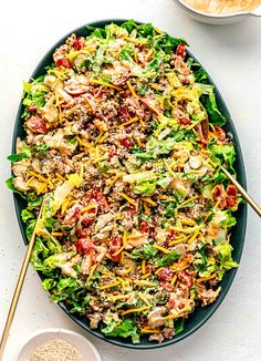 a salad with meat and vegetables in a bowl next to some chopsticks on the side