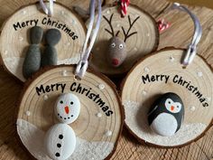 four christmas ornaments with snowmen, penguins and reindeers on them hanging from wood slices