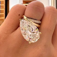 a person's hand holding a ring with a pear shaped diamond on it and two bands around the band