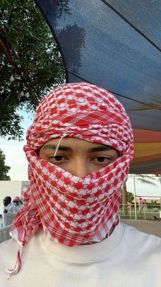 a man wearing a red and white checkered bandana over his head with an umbrella in the background