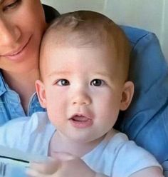 a woman holding a baby in her arms and looking at the camera with an excited look on her face