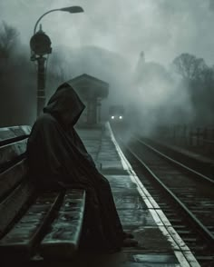 a person sitting on a bench in front of a foggy train station at night