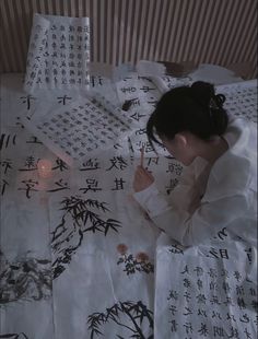 a woman sitting on top of a bed holding a pen and writing in chinese characters