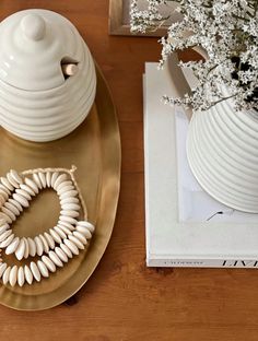 a white vase sitting on top of a wooden table next to a plate with shells