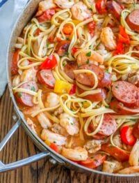 a skillet filled with pasta, shrimp, and peppers on top of a wooden table