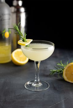 a drink in a coupe glass with lemons and rosemary garnish