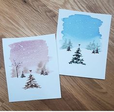 two cards with watercolor trees on them sitting on a wooden table next to each other