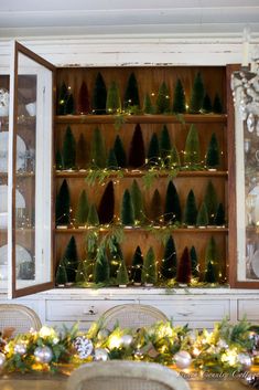 christmas trees are arranged on the back of an old china cabinet in a dining room