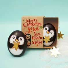 two penguins are sitting in an egg box and one is holding a star, the other has a christmas card