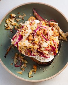 an open face sandwich with red onions and other toppings in a green bowl on a white table